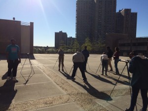 The sun casts long shadows behind students as they practice setting up and focusing brand new telescopes.