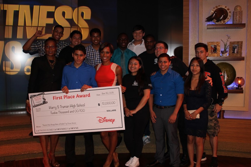 Oscar Anzora receives his award check from ABC 7 Eyewitness News anchor Sade Baderinwa, surrounded by his classmates.